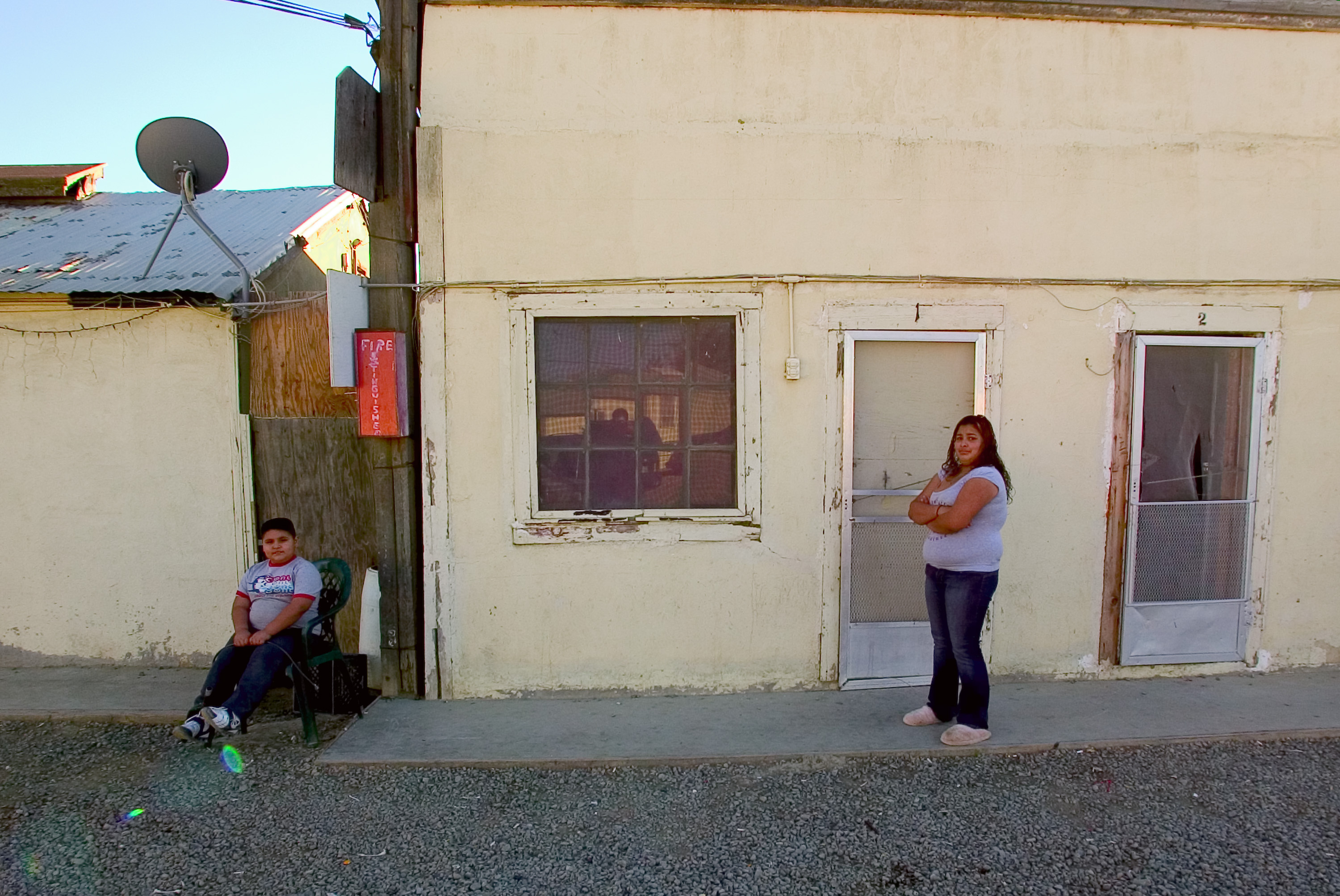 Two children wait outside a migrant encampment in Huron, California while their parents pick lettuce. 2007